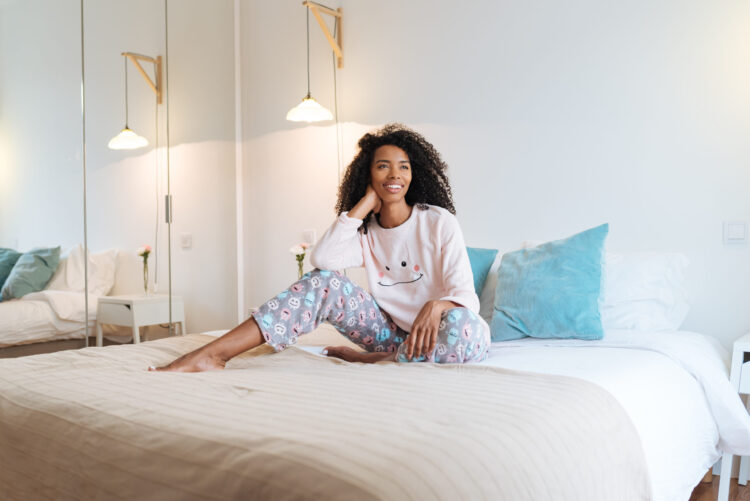 Mulher com pijama sobre a cama bem disposta em alusão aos benefícios de tomar melatonina