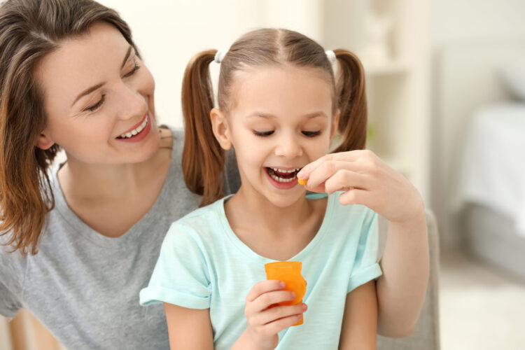 Mãe visualizando sua filha comendo uma fruta em alusão aos benefícios que uma dieta nutritiva associada ao Gummy Kids tem.