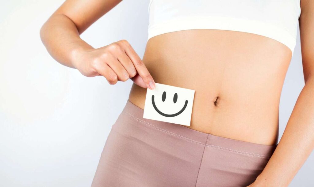 Pessoa mostrando a barriga e uma placa com um sorriso desenhado representando um intestino saudável.