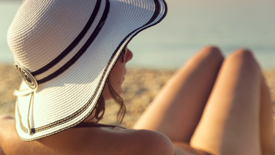 Mulher de chapéu de palha e óculos escuros pegando sol na praia.