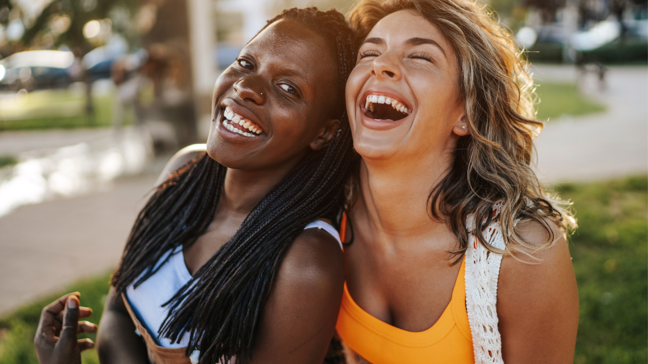 Duas mulheres sorrindo, sendo uma negra e outra branca.