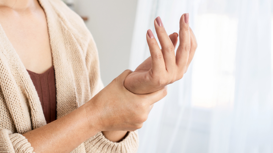 Mulher segurando uma de suas mãos representando dor nos ósseos e articulações.
