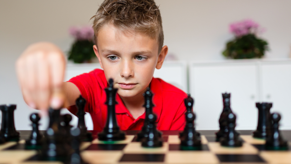 Menino branco de olhos azuis, usando camisa vermelha, jogando xadrez.