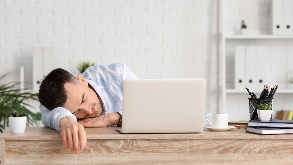 Homem com aparência de cansado ao lado de um computador.