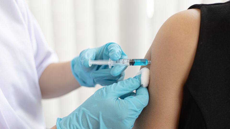 imagem mostra braço de uma pessoa e mãos de profissional da saúde aplicando vacina