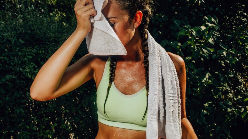 Mulher com roupa de academia enxugando suor com uma toalha. Formas de ganhar mais energia e disposição.