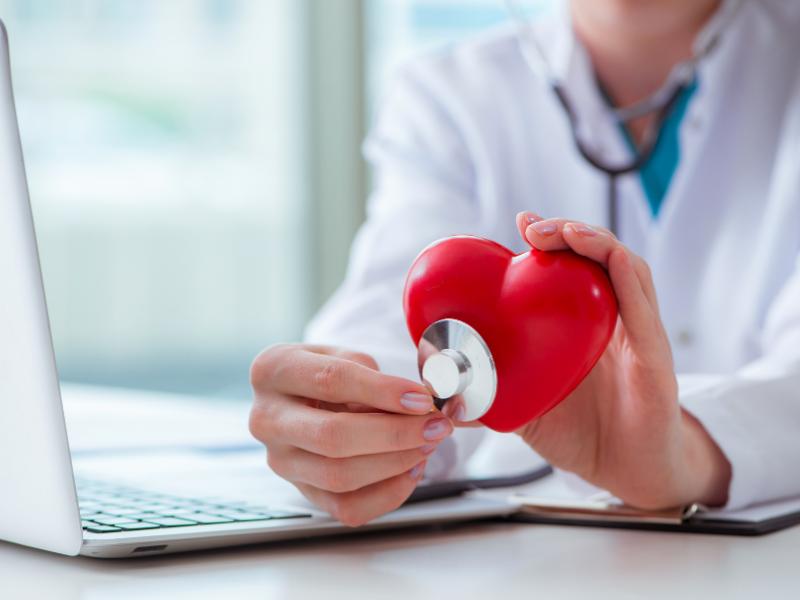 Imagem de médico examinando coração de borracha representando especialidade em cardiologia.